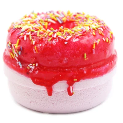 A large circular bright red doughnut shaped bath bomb that has some various different coloured sprinkles embedded on top of it, , on a white background.