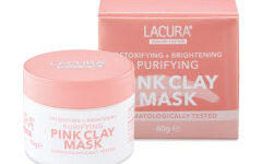 A short cylindrical bright white glass jar with a metallic pink lid that has Aldi Lacura Pink Clay Mask written in bright pink writing on it next to a pale pink cardboard box that has Aldi Lacura Pink Clay Mask written in bold white writing on it, on a white background.