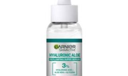 A short rounded cylindrical clear glass bottle full of some clear liquid with a white rubber pipette lid and a gradient green and silver label that has Garnier written in bold black writing, and Skin Active Hyaluronic Aloe Replumping Super Serum written in dark green writing on it, on a white background.