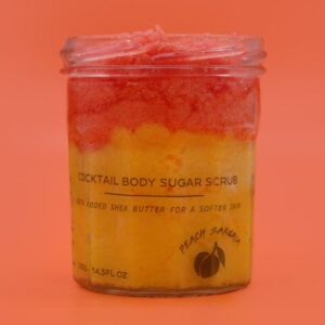 A medium cylindrical clear glass jar full of some bright red and yellow sugar scrub with a metallic silver lid that has H&L Bath Bombs Peach Sangria Fragranced Sugar Body Scrub written in bold black writing on it, on a white background.