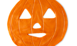 A large bright orange Jack-O[-Lantern shaped block of shower jelly that has some eye holes, a nose hole, and a mouth hole cut out of it, on a white background.