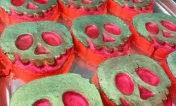 A large gradient bright green and red apple shaped bath bomb that has a gold skull face engraved on it, on a white background.