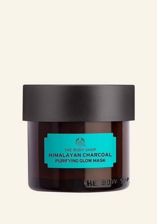 A short cylindrical black glass jar with a black plastic lid and a dark green label that has The Body Shop Himalayan Charcoal Purifying Glow Mask written in bold black writing on it, on a white background.