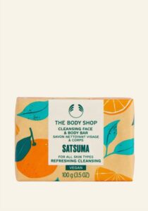 A large rectangular block of Soap wrapped in some bright white paper that has The Body Shop Satsuma Cleansing Face & Body Bar written in bold black writing and some pictures of some bright orange satsumas on it, on a white background.