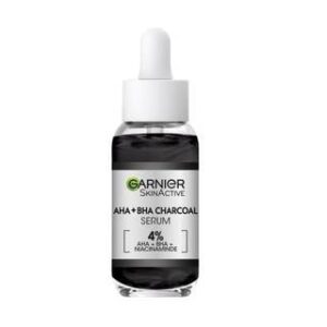 A short rounded cylindrical clear glass bottle full of some black liquid with a white rubber pipette lid and a silver label that has Garnier Skin Active 4% AHA + BHA & Niacinamide Charcoal Serum written in bold black writing on it, on a white background.