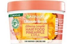 A short cylindrical white plastic tub with a bright green lid and a bright green label that has Garnier Ultimate Blends Hair Food Pineapple & Amla 3-in-1 Hair Treatment Mask written in bold black writing and a picture of a Pineapple on it, on a white background.