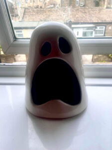 A large bright white ghost’s head shaped candle holder on a large rectangular glossy white windowsill.
