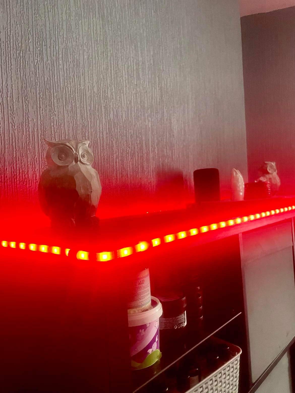 Luke Loves Autumn 2022 | How I've Decorated My Room This Year A large rectangular black wooden cabinet covered in some bright red fairy lights that has a large dark grey resin Owl ornament at one end of it, a large rectangular white plate that has a thin dark grey Owl Ornament next to a short cylindrical clear glass bowl full of some various different coloured sweets on top of it, and a large dark grey resin owl ornament at the other end of it on a white background.