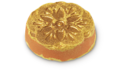 A large circular bright yellow and orange Bath Bomb that has an intricate diamond pattern and some gold Lustre embedded on it, on a white background.