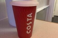 A tall cylindrical red ceramic cup with a white rubber lid that has Costa engraved in bold white writing on it, on a white background.