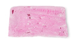 A small bright pink rectangular block of soap that has some bright white cornflower on top of it, on a white background.