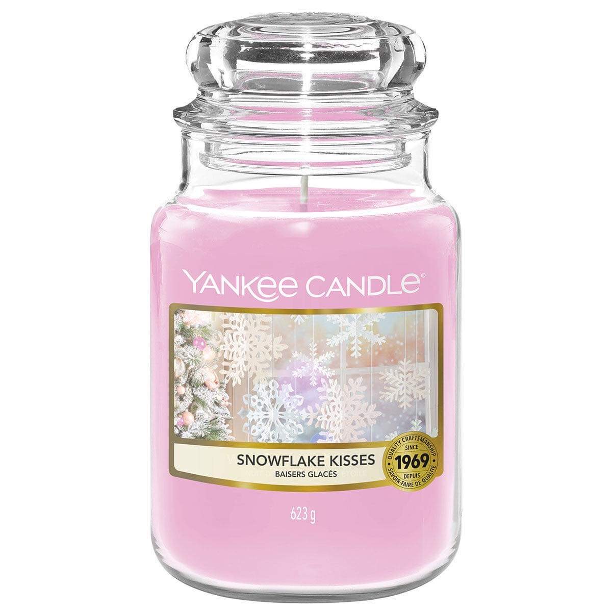 What I Thought of the Yankee Candle Advent House 2014 A tall cylindrical glass jar full of some pale pink wax with a label that has Yankee Candle written in white writing, snowflake kisses written in black writing, and some pictures of some white falling snowflakes on it, on a white background.