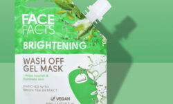 A tall rectangular gradient green and white plastic pouch with a white plastic lid that has Face Facts Brightening Green Tea Jelly Wash-Off Face Mask written in bold black writing and a picture of a bright green Face Mask on it, on a white background.