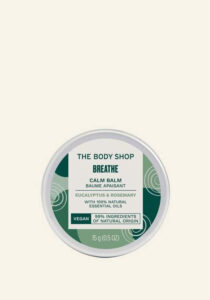 A small circular metallic white Tin with a gradient green and white label that has The Body Shop Breathe Calm Balm written in dark green writing on it, on a white background.