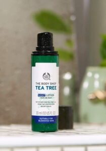 A short cylindrical bright green plastic bottle with a bright white label that has The Body Shop Tea Tree Night Lotion written in dark green writing on it, on a white background.