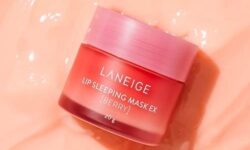 A short cylindrical clear plastic jar full of some bright pink liquid with a bright pink plastic lid that has Laneige Berry Lip Sleeping Mask written in bright white writing on it, on a white background.