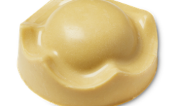A large golden caramel crown shaped block of solid body butter that has a large dome coming out of the top of it, on a white background.