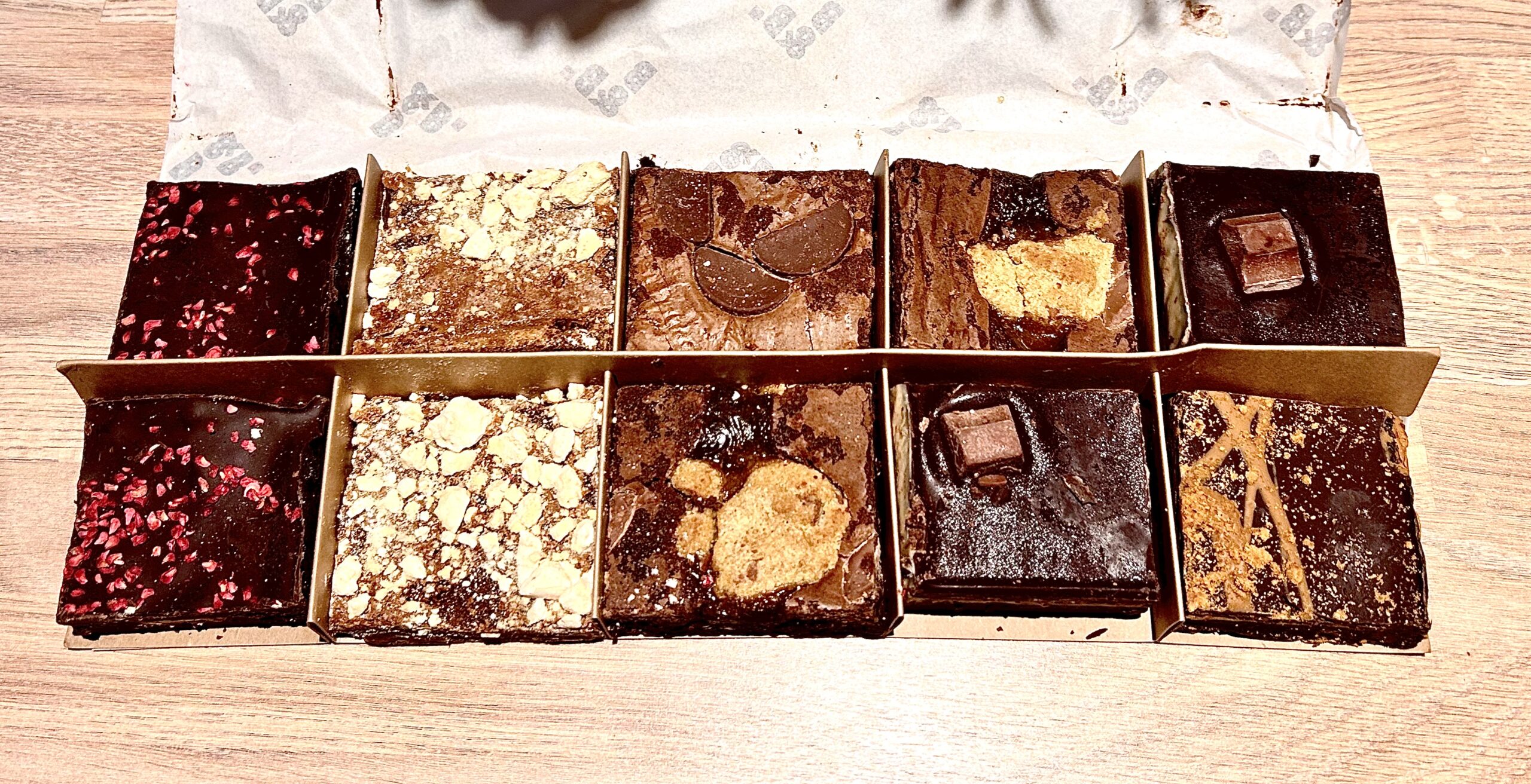 The Best Selection Of Brownies In Leeds | Brown & Blond Choose Your Own Brownie Box A collection of eight medium rectangular dark brown chocolate brownies next to two medium rectangular pale white blondies inside a large light brown rectangular cardboard box, on a white background.