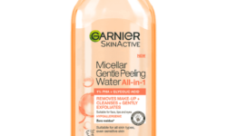 A tall rounded rectangular bright peachy pink plastic bottle with a bright peachy pink plastic lid that has Garnier SkinActive written in bold black writing and Micellar Gentle Peeling Water written in dark pink writing on it, on a white background.