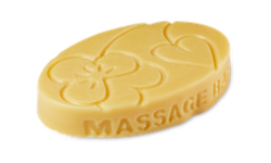 A medium golden yellow oval shaped block of solid massage oil that has some pictures of some Violet Flowers engraved on it, on a white background.
