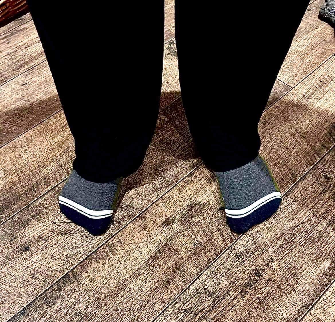 Me wearing a pair of fluffy dark green socks that has Box Menswear written in bold white writing on them stood on a light wooden laminate floor.