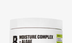 A short cylindrical white Plastic Tub with a white Plastic Lid that has By Beauty Bay Moisture Complex + Algae written in bold black writing and Face Mask written in dark purple writing on it, on a white background.