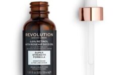 A short cylindrical brown glass bottle with a gold and white Rubber Pipette Lid and a black label that has Revolution Skincare 0.5% Retinol & Rosehip Seed Oil Smoothing Serum written in bright white writing on it, on a white background.