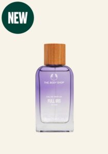 A tall rectangular clear glass bottle full of some translucent yellow liquid with a light wooden Lid that has The Body Shop Full Iris Eau De Parfum written in bold white writing on it, on a white background.