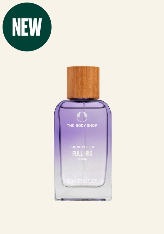 A tall rectangular clear glass bottle full of some translucent yellow liquid with a light wooden Lid that has The Body Shop Full Iris Eau De Parfum written in bold white writing on it, on a white background.