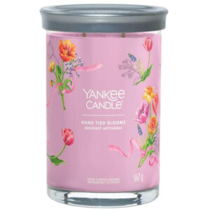 A tall cylindrical glass jar full of some bright pink wax with a label that has Yankee Candle written in white writing, Hand Tied Blooms written in black writing, and a picture of some different coloured Flowers on it, on a white background..