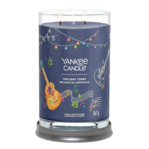 A tall cylindrical glass jar full of some bright blue wax with a label that has Yankee Candle written in white writing, Twilight Tunes written in black writing, and a picture of a Guitar on it, on a white background..
