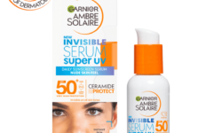 A short cylindrical bright white Glass Bottle with a metallic white pump lid that has Garnier written in bold black writing, Ambre Solaire Super UV Daily Invisible Face Serum written in dark blue writing, and SPF 50+ written in bright orange writing on it, on a white background.