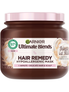 A short cylindrical brown Plastic Tub with a metallic pink Plastic Lid and a metallic pink label that has Garnier Ultimate Blends Delicate Oat Milk Hair Remedy Hypoallergenic Mask written in bold black writing on it, on a white background.
