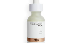 A short cylindrical clear glass bottle full of some dark green liquid with a white rubber pipette lid and a white label that has Revolution Skincare written in bright silver writing and Cica Serum written in bold black writing on it, on a white background.