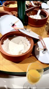 Several short cylindrical terracotta pots full of some creamy white body butter on top of a large circular light wooden table.
