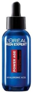 A short rounded cylindrical clear glass bottle full of some clear liquid with a black rubber pipette lid and a dark blue label that has L’Oreal Paris Men Expert Power Age hyaluronic Acid Serum written in bright white writing on it, on a white background.