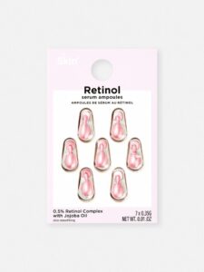 seven small teardrop shaped plastic ampoules full of some clear liquid encased in some clear plastic on a medium rectangular piece of white cardboard that has Primark PS… Skin + Retinol Serum Ampoules written in bold black writing on it, on a white background.