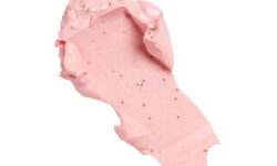 A medium circular puddle of some bright pink face mask that has some pieces of Sugar Sprinkles running through it, on a white background.
