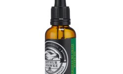 A short cylindrical brown glass bottle with a black rubber pipette lid and a black label that has Arthur J Hawke Jamaican Me Crazy Beard Oil written in bold white writing and a picture of a black and white hawk on it, on a white background.