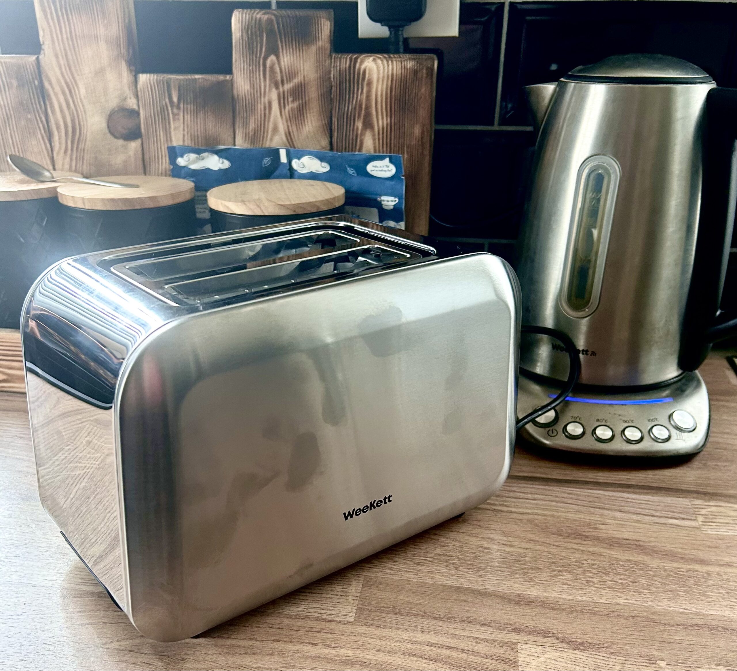 Pop Goes The Toaster | WeeKett Matching 2 Slices Toaster | Gifted A large rectangular shiny silver metal Toaster that has WeeKett written in bold black writing on it next to a tall cylindrical silver matte plastic kettle with a black matte plastic handle that has WeeKett written in bold black writing on it on a light wooden worktop.