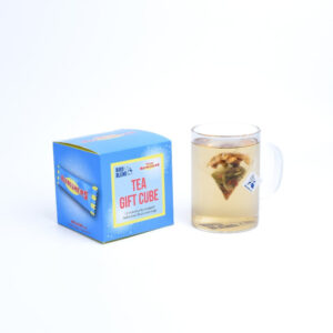 A large square bright blue and yellow cardboard box with a creamy white label that has Bird & Blend Tea Company x Swizzles Refreshers Tea Cube written in bright yellow writing on it next to a short cylindrical clear glass mug full of some bright yellow liquid, on a white background.