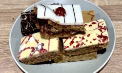 A collection of six medium rectangular golden brown pieces of Flapjack on a small circular light grey plate, on a white background.