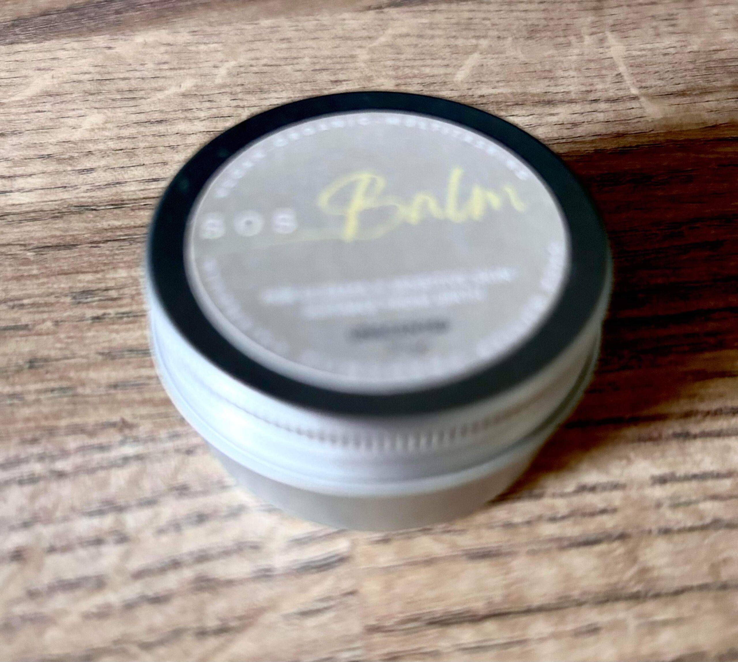 Nothing Else Can Save Me, S.O.S. | SOS Balm Unscented Balm | Gifted A short cylindrical silver metal tin with a silver metal lid and a white label that has SOS Balm Unscented Balm written in bold black writing on it, on a white background.