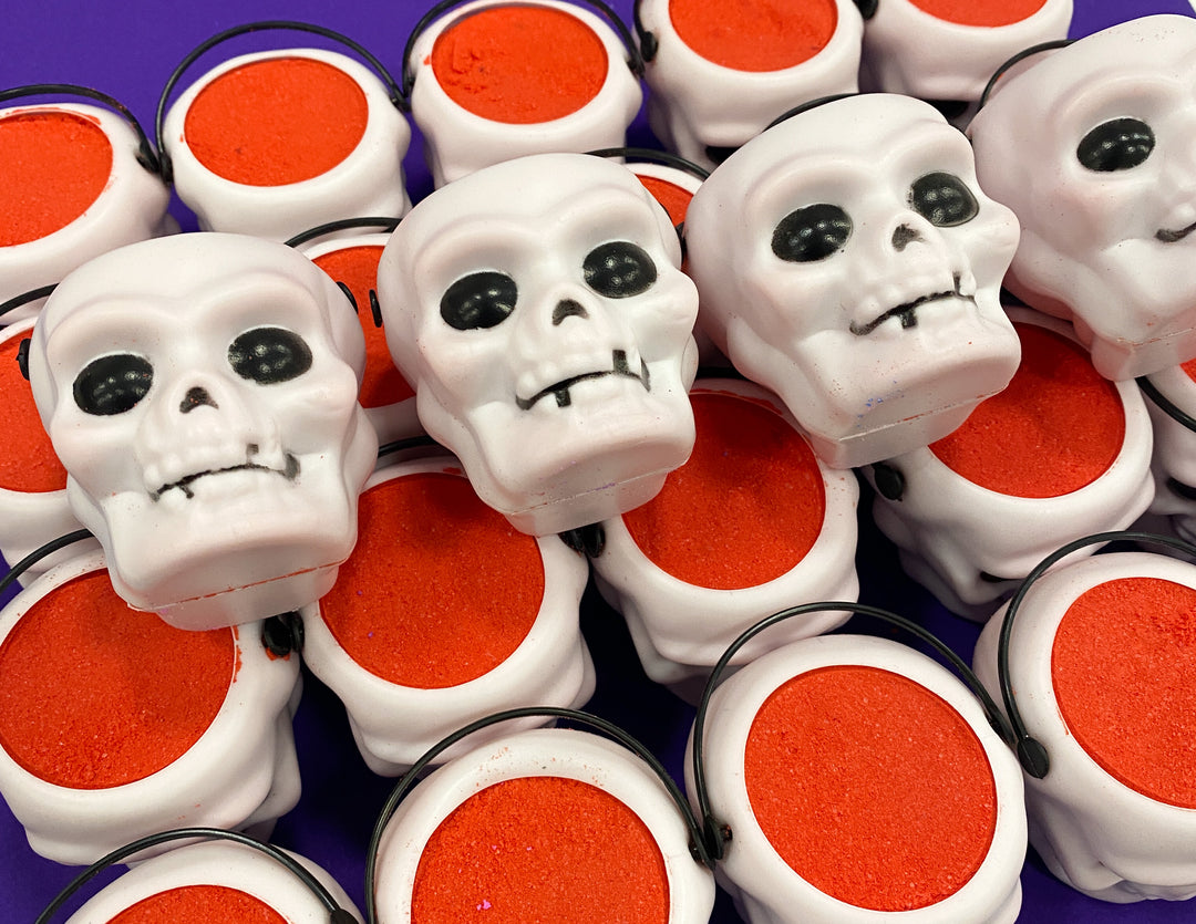A pile of some small bright white skull shaped bath bombs that all have some black eyes engraved on them, on a white background.