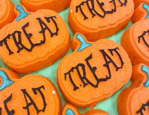 A large bright Orange Pumpkin Shaped Bath Bomb that has Treat written in bold black writing on it, on a white background.