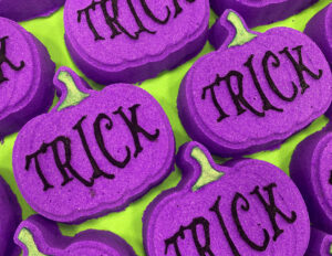 A large dark Purple Pumpkin shaped Bath Bomb that has Treat written in bold black writing on it, on a white background.
