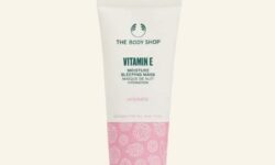 A tall conical gradient bright pink and white plastic tube with a dark green plastic lid that has The Body Shop Vitamin E Moisture Sleeping Mask written in dark green writing on it, on a white background.