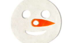 A large circular bright white snowman’s head shaped block of Shower Jelly that has a bright orange carrot nose engraved on it and some Eye holes, a nose hole, and a mouth hole cut out of it, on a white background.