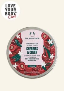 A short cylindrical bright white plastic tub with a bright white plastic lid and a bright pink label that has The Body Shop Cherries & Cheer Body Butter written in dark green writing and a picture of some bright Red Cherries on it, on a white background.