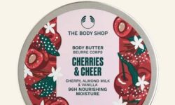 A short cylindrical bright white plastic tub with a bright white plastic lid and a bright pink label that has The Body Shop Cherries & Cheer Body Butter written in dark green writing and a picture of some bright Red Cherries on it, on a white background.
